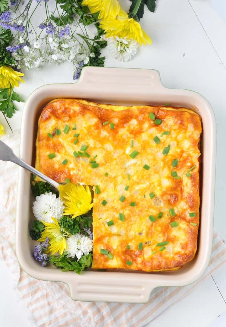 An overhead shot of a ham and cheese omelet in a baking dish with flowers at the side