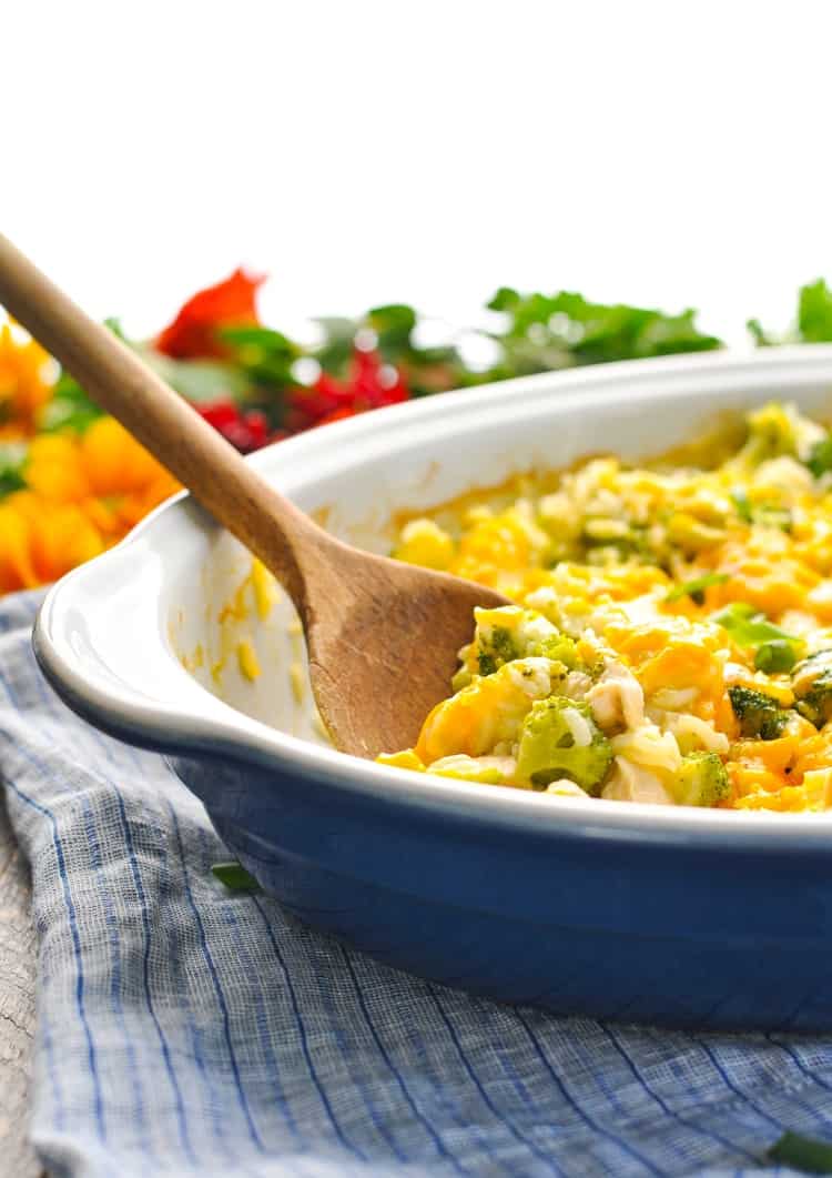 An oval casserole dish with a chicken broccoli rice casserole inside and a wooden spoon