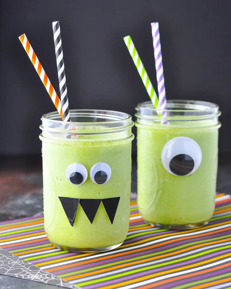 Two glass jars filled with a monster green smoothie and topped with colored straws