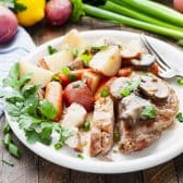 Square side shot of easy slow cooker pork chops served on a white plate with potatoes, vegetables, and gravy.