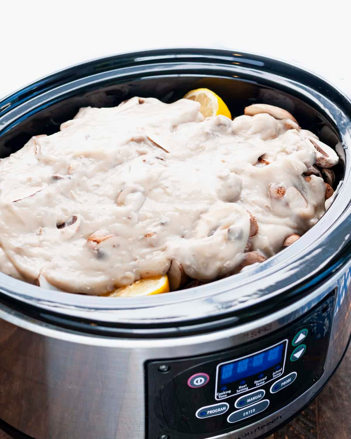 Cream of mushroom soup on top of mushrooms and pork chops in a slow cooker.