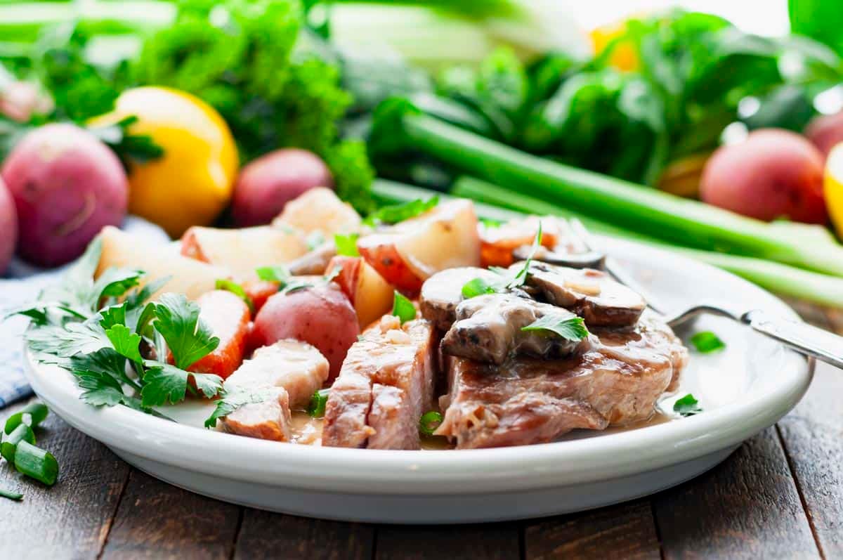 Horizontal side shot of a white plate full of easy Crock Pot pork chops with vegetables and gravy.