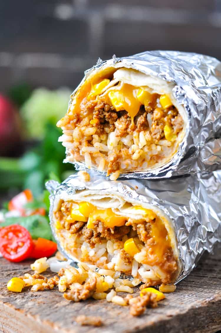 Stacked beef burritos on a board with melted cheese