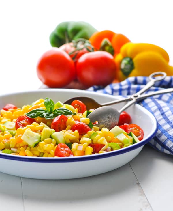 A side-angled view of a large bowl of fresh corn salad with tomatoes, zucchini, and onions.