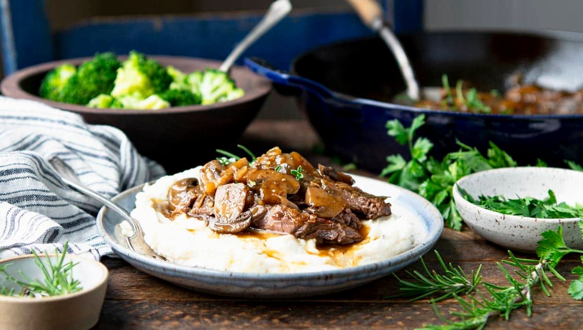 Horizontal image of a plate of round steak with gravy and mashed potatoes.