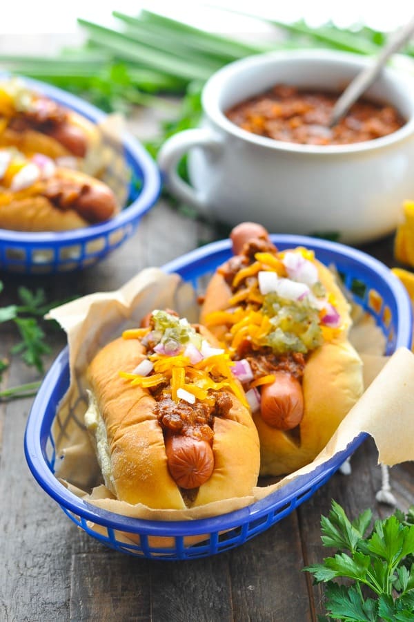 Close front shot of chili dogs in a basket with pot of hot dog chili in the background