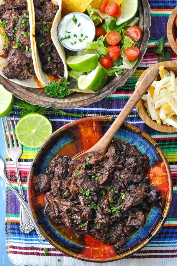 Beef barbacoa in a bowl on a table with Mexican sides