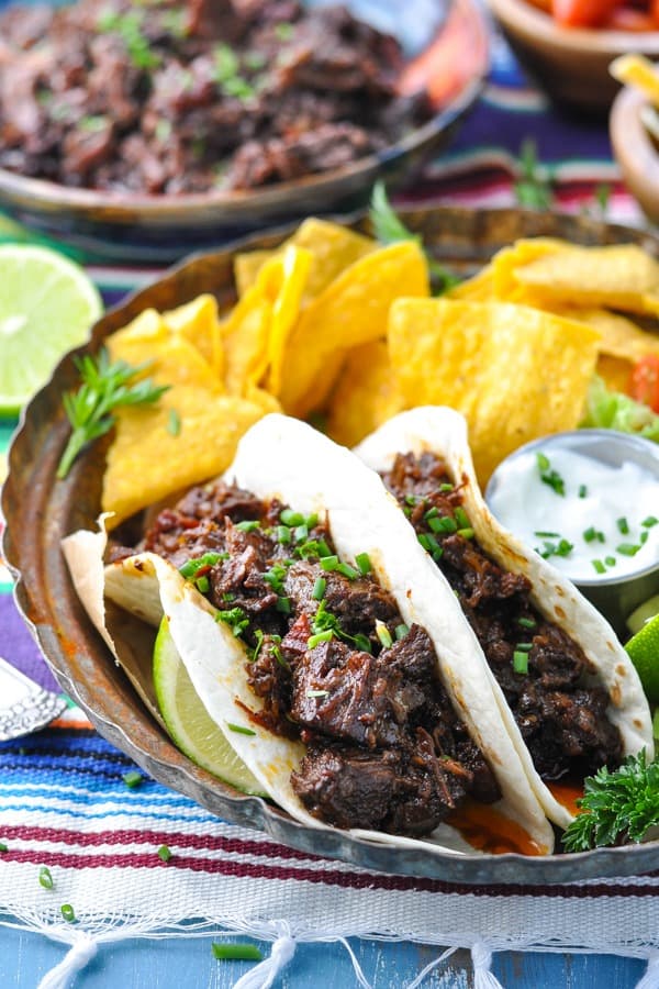 Front shot of beef barbacoa soft tacos on a plate with tortilla chips