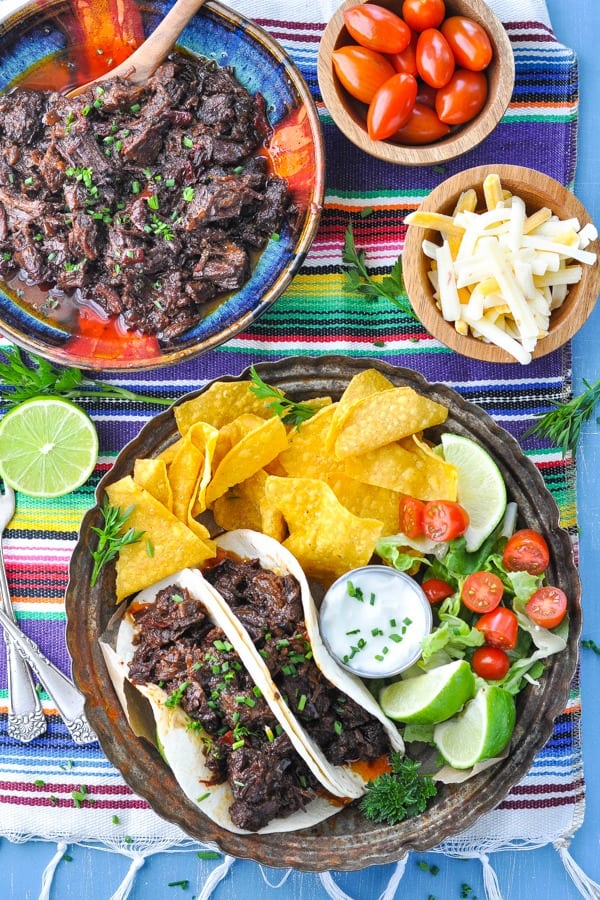 Overhead shot of beef barbacoa on a table with limes and a striped placemat