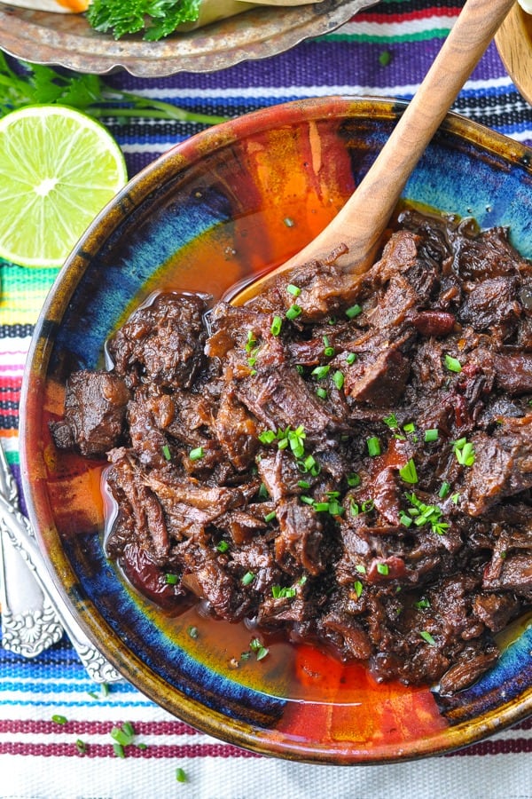 Close overhead shot of beef barbacoa in a bowl with a wooden serving spoon