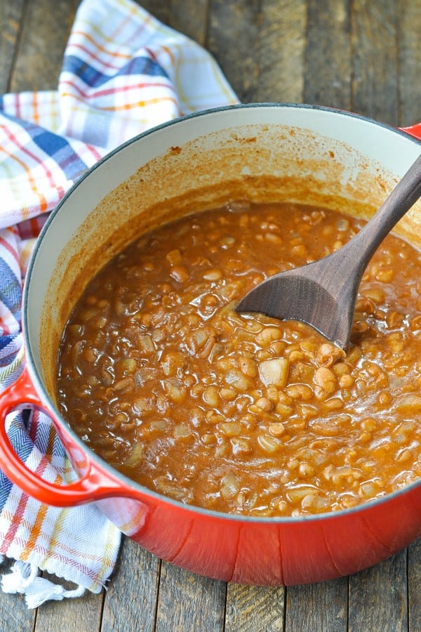 Ranch style beans in a red dutch oven with a wooden spoon