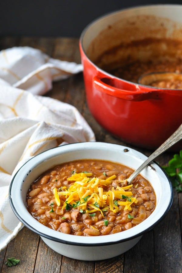 Ranch style beans in a white bowl with a red Dutch oven in the background