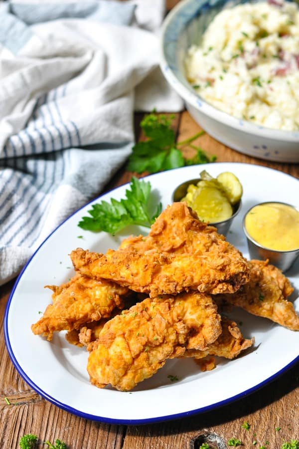 Serving platter of fried chicken tenders with pickles and honey mustard dip