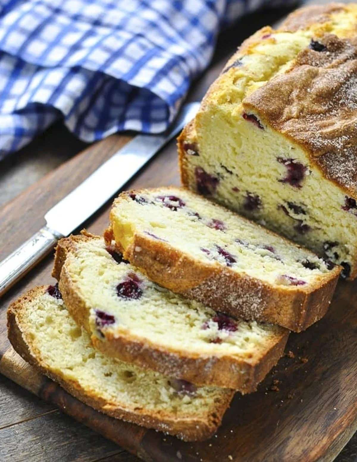 Sliced loaf of blueberry bread on a wooden cutting board.