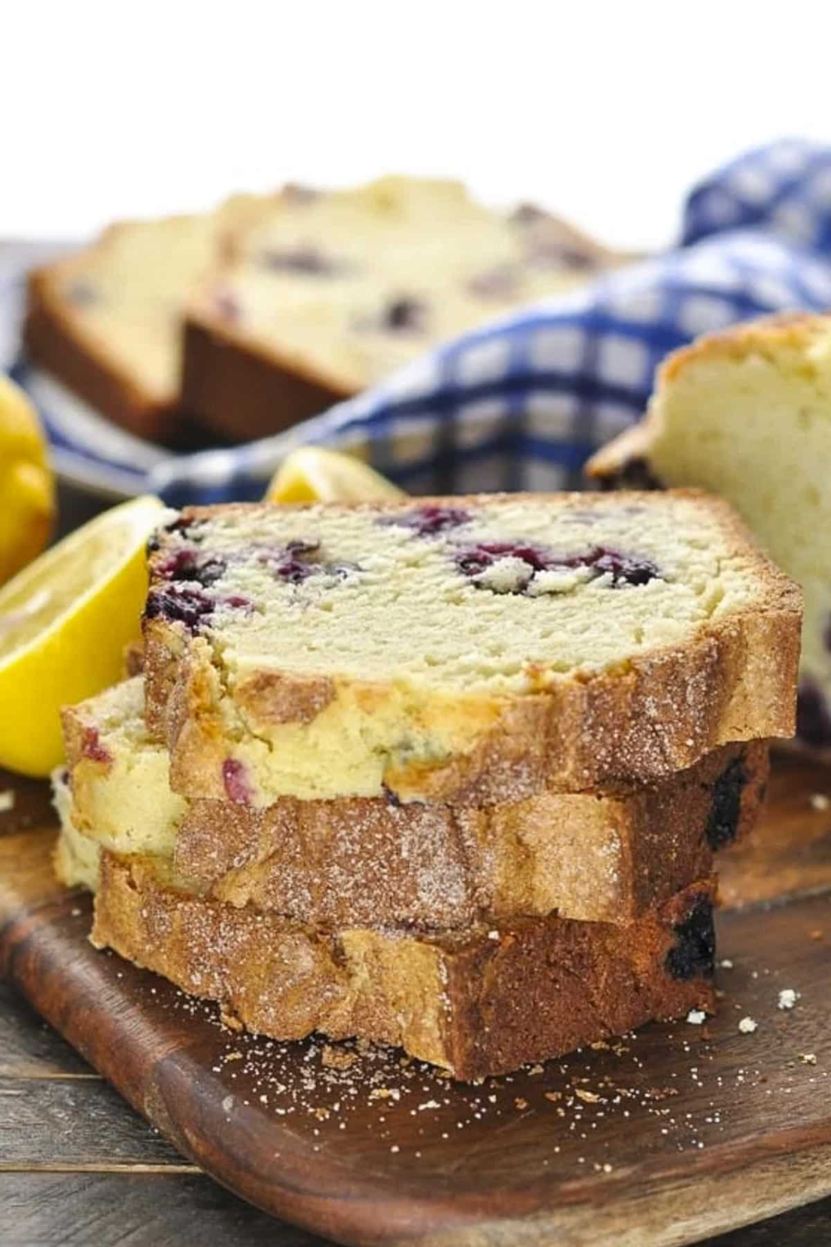 Stack of slices of moist blueberry bread on a wooden cutting board.