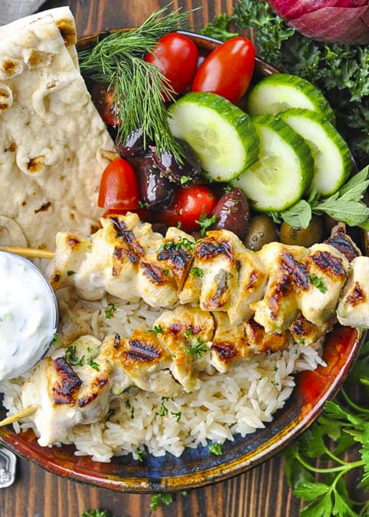 Overhead shot of chicken souvlaki in a bowl with rice, veggies, and pita.