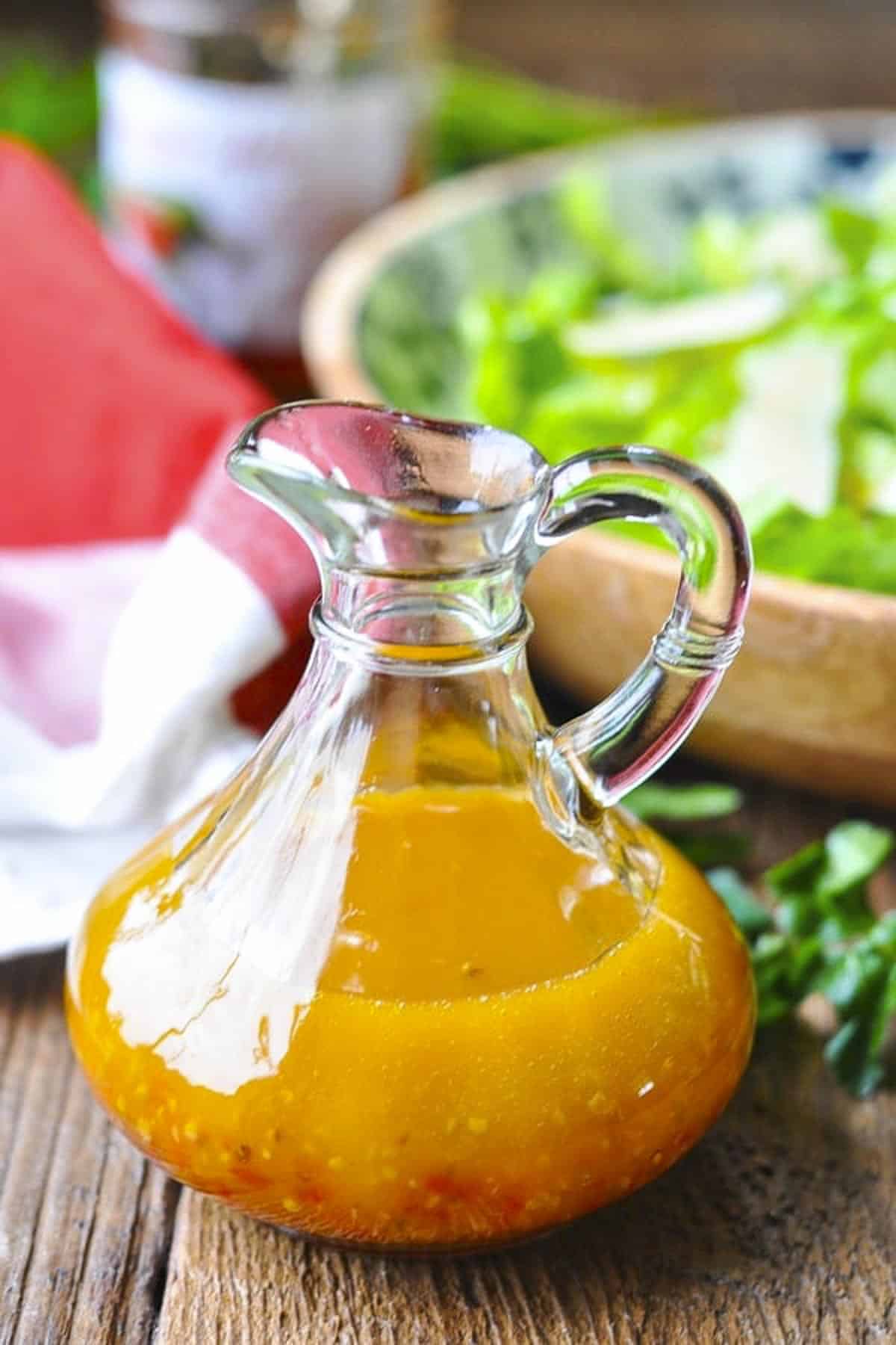 Bottle of homemade pepper jelly vinaigrette recipe on a wooden table with salad in the background.