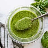 Overhead horizontal image of a spoon in a jar of pesto.