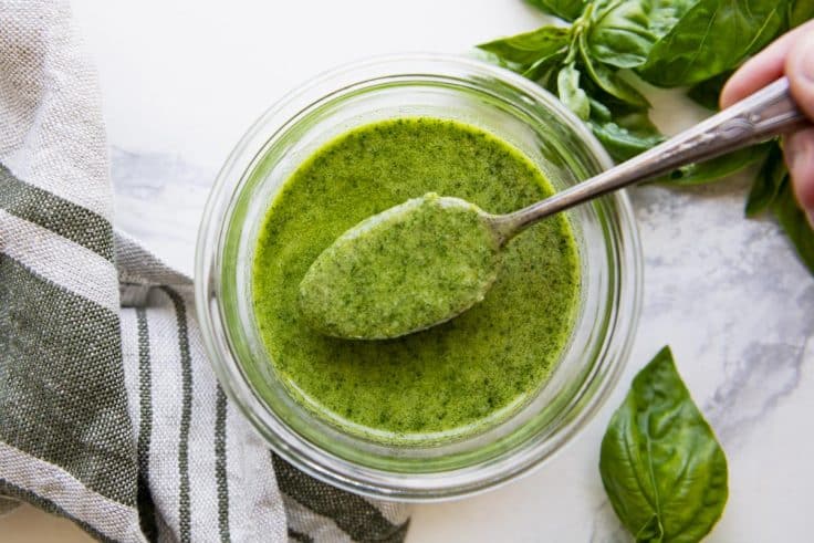 Overhead horizontal image of a spoon in a jar of pesto.