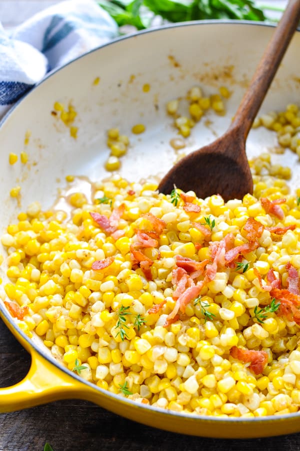 Close up front shot of fried corn with bacon in a cast iron skillet with a wooden spoon