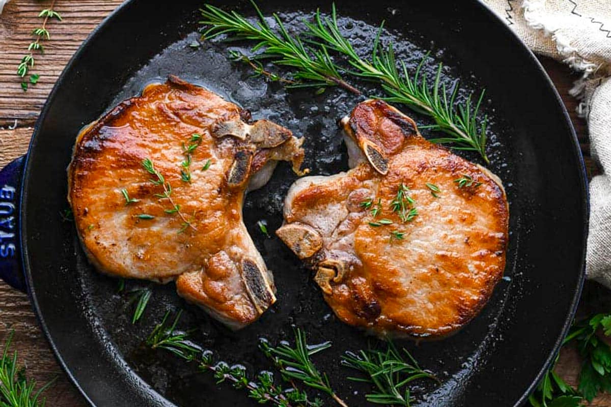 Horizontal overhead image of the best pork chop brine recipe on pork chops in a cast iron skillet.
