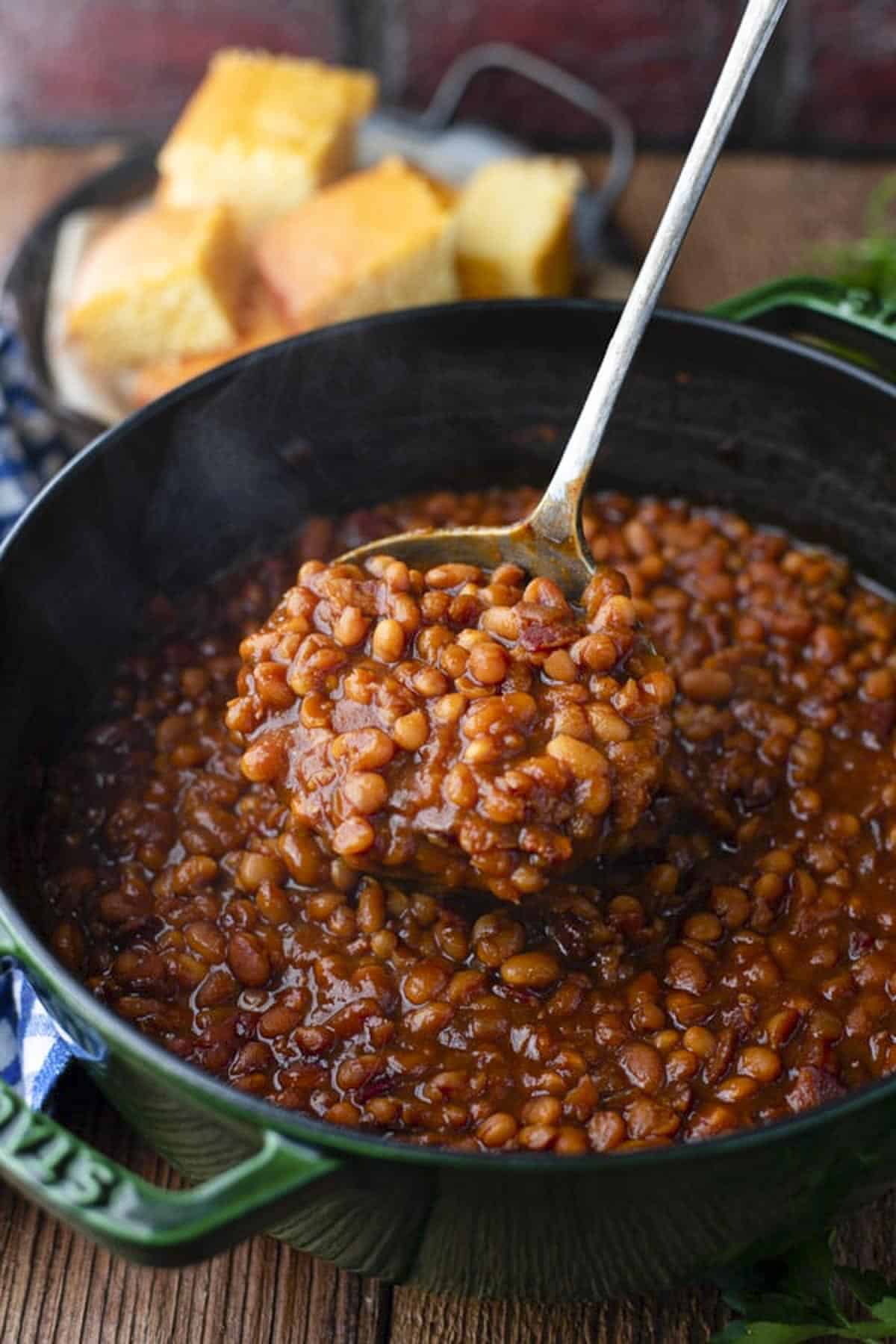 Side shot of a ladle serving homemade baked beans from scratch with a side of cornbread.