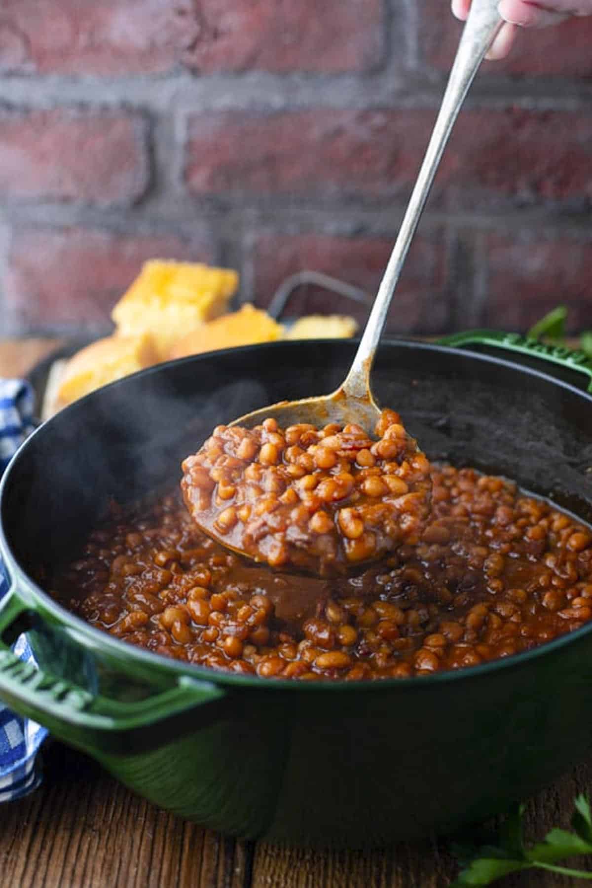 Ladle serving homemade baked beans from a Dutch oven.