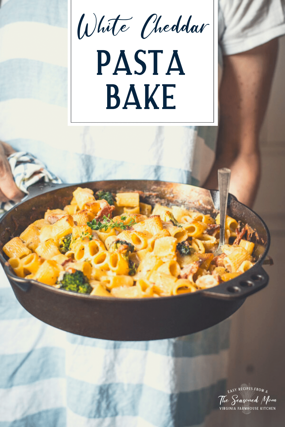 Hands holding a skillet of cheesy pasta bake with text title overlay