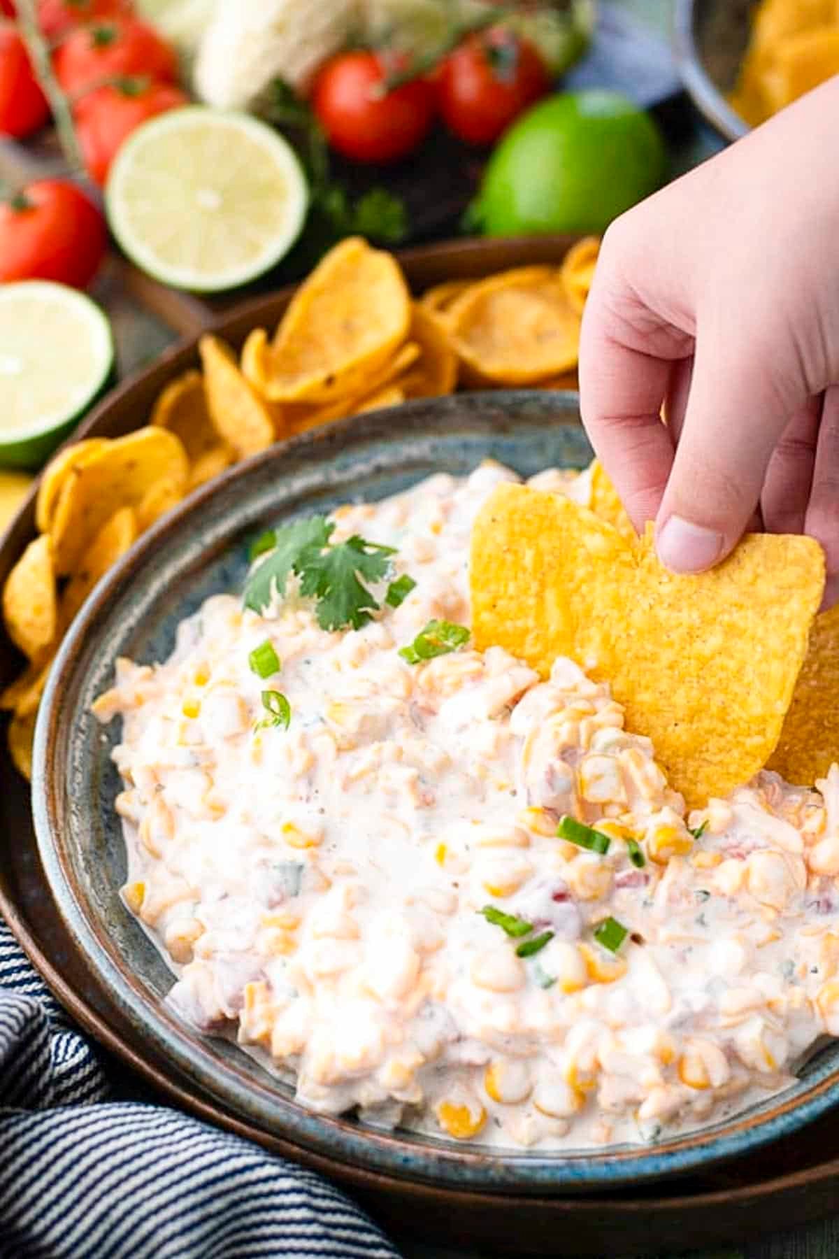 Hand scooping up cold corn dip with a tortilla chip.