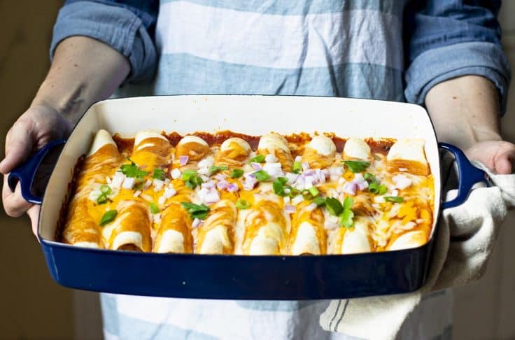 Horizontal side shot of hands holding a pan of easy chicken enchiladas.