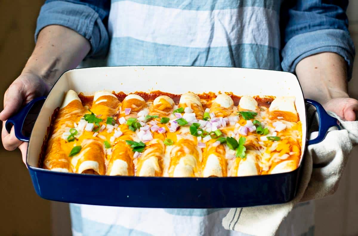 Horizontal side shot of hands holding a pan of easy chicken enchiladas.