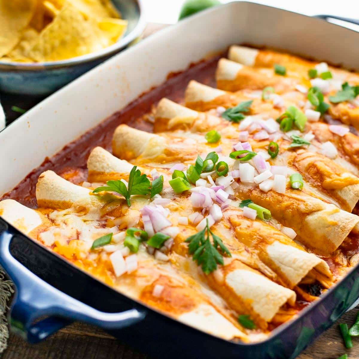 Square front shot of easy chicken enchiladas in a baking dish.
