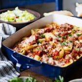 Square front shot of stuffed shells with meat in a blue baking dish.
