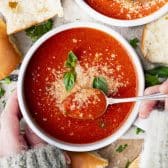 Horizontal overhead image of hands eating a bowl of the best tomato basil soup recipe with a spoon.