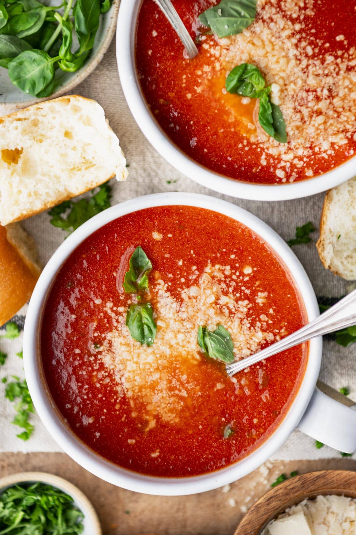 Overhead shot of bowls of the best tomato basil soup recipe served with bread on the side.