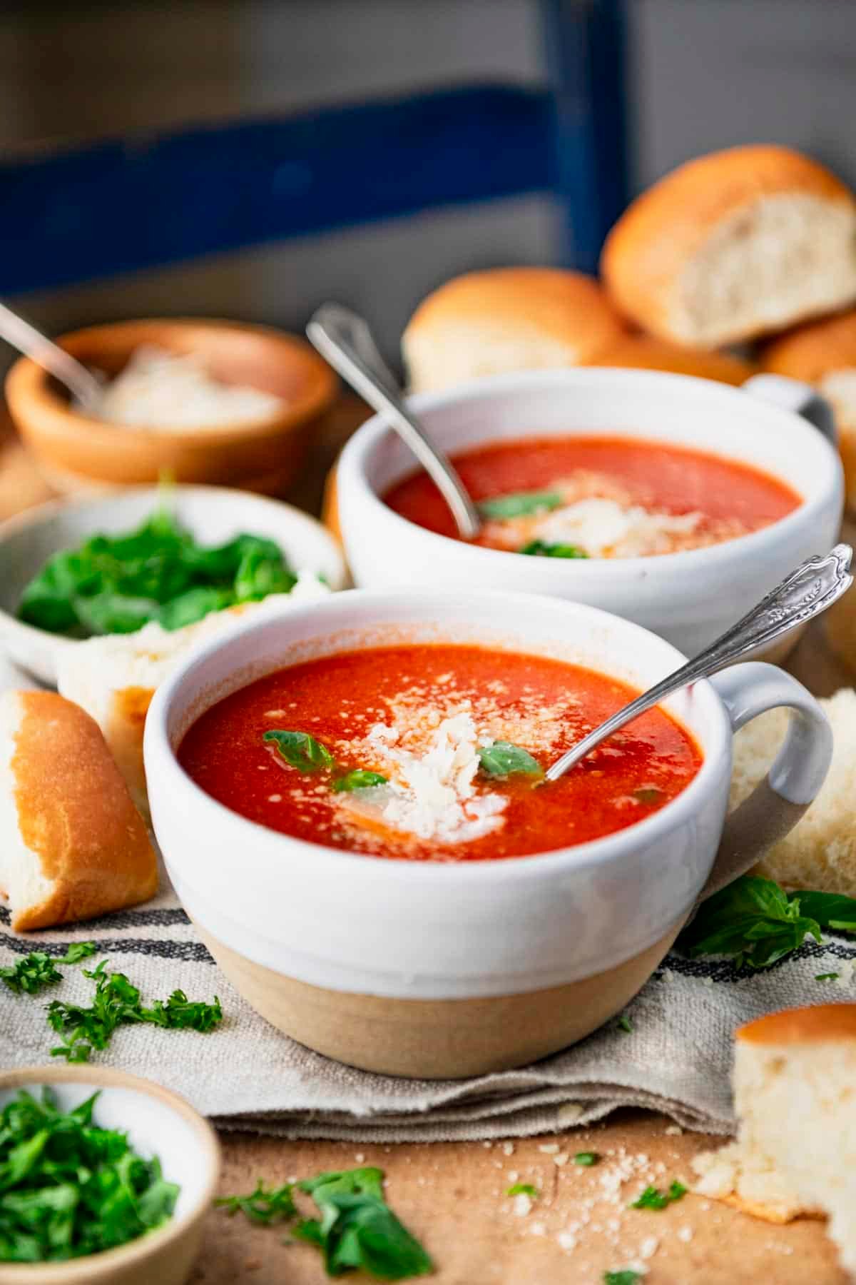 Side shot of two bowls of creamy tomato basil soup with parmesan and fresh basil on top.