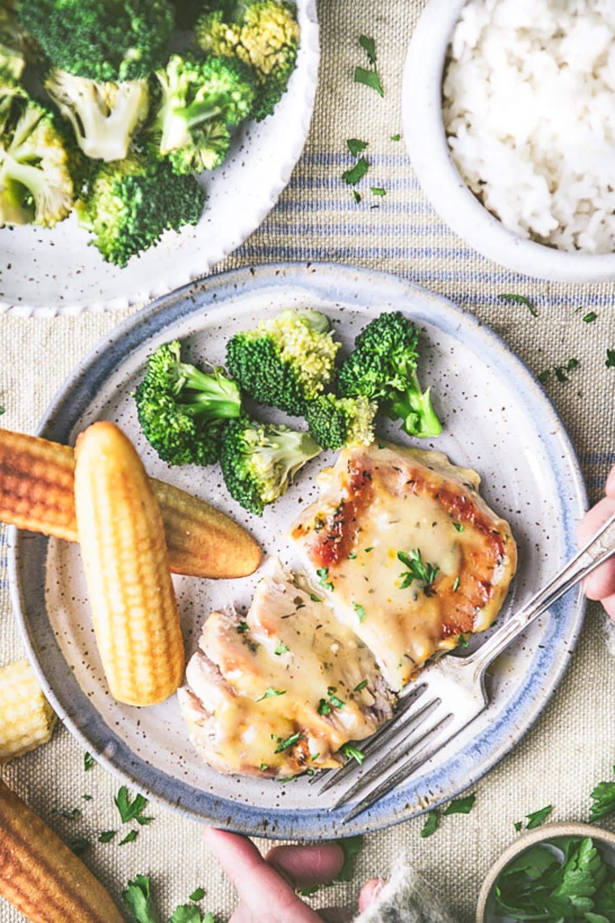 Overhead shot of hands eating ranch pork chops on a plate with a side of broccoli.