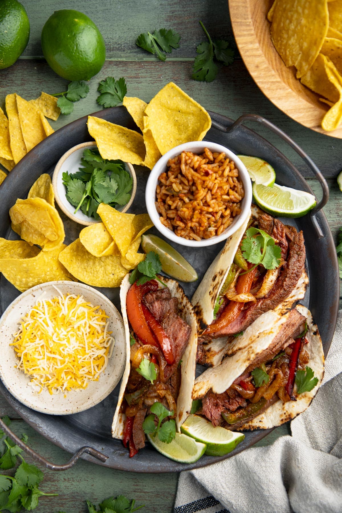 Close overhead image of a metal plate full of sheet pan steak fajitas with a side of rice and chips.