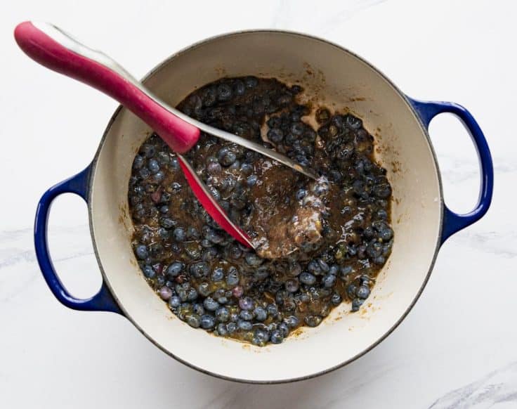 Mashing blueberries with a potato masher in a Dutch oven.