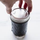 Tightening lids and bands on jar of blueberry jam.