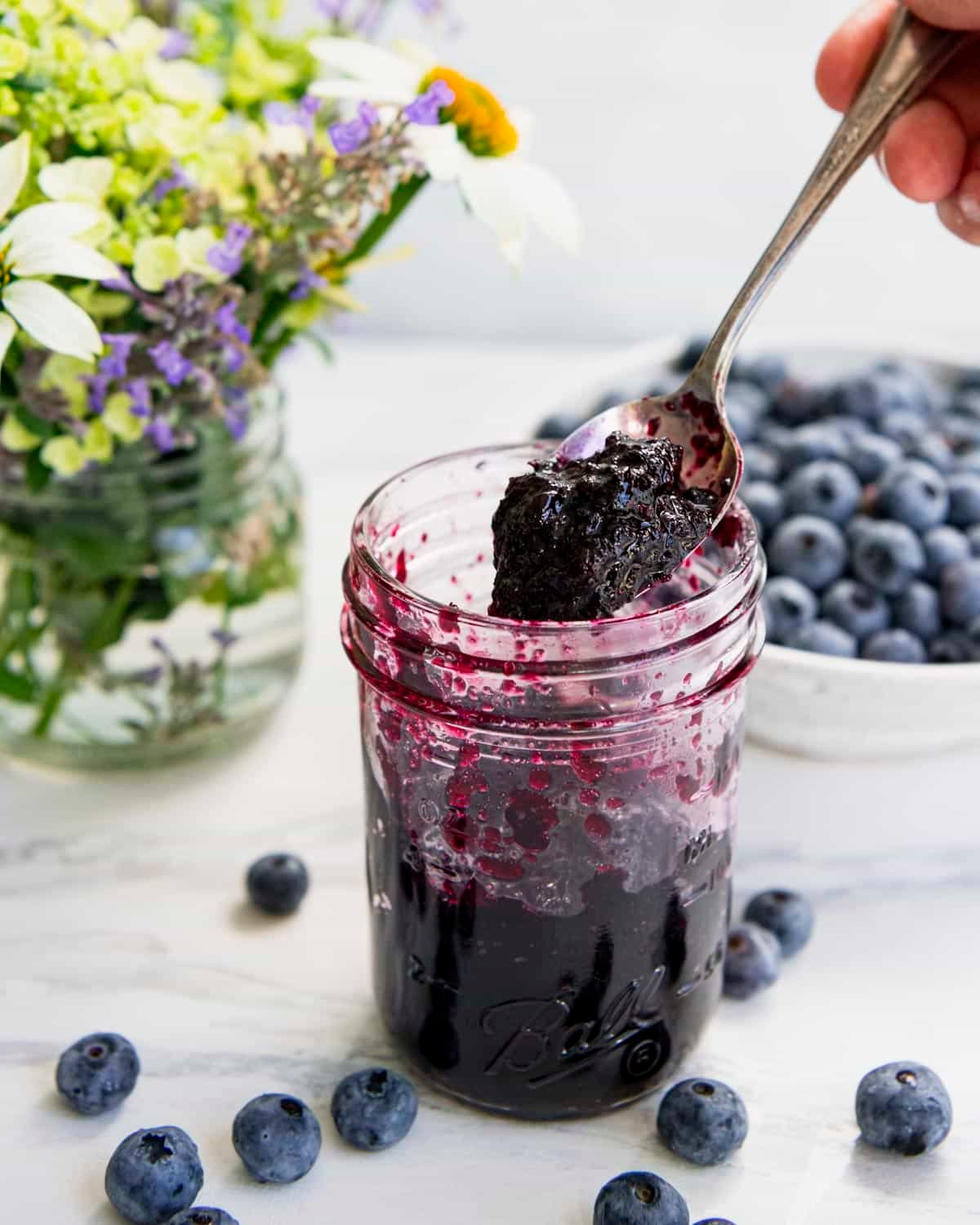 Hand serving homemade blueberry jam without pectin from a mason jar.