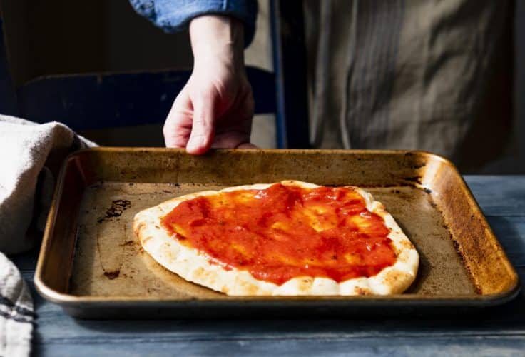 Spreading pizza sauce on a naan flatbread pizza.