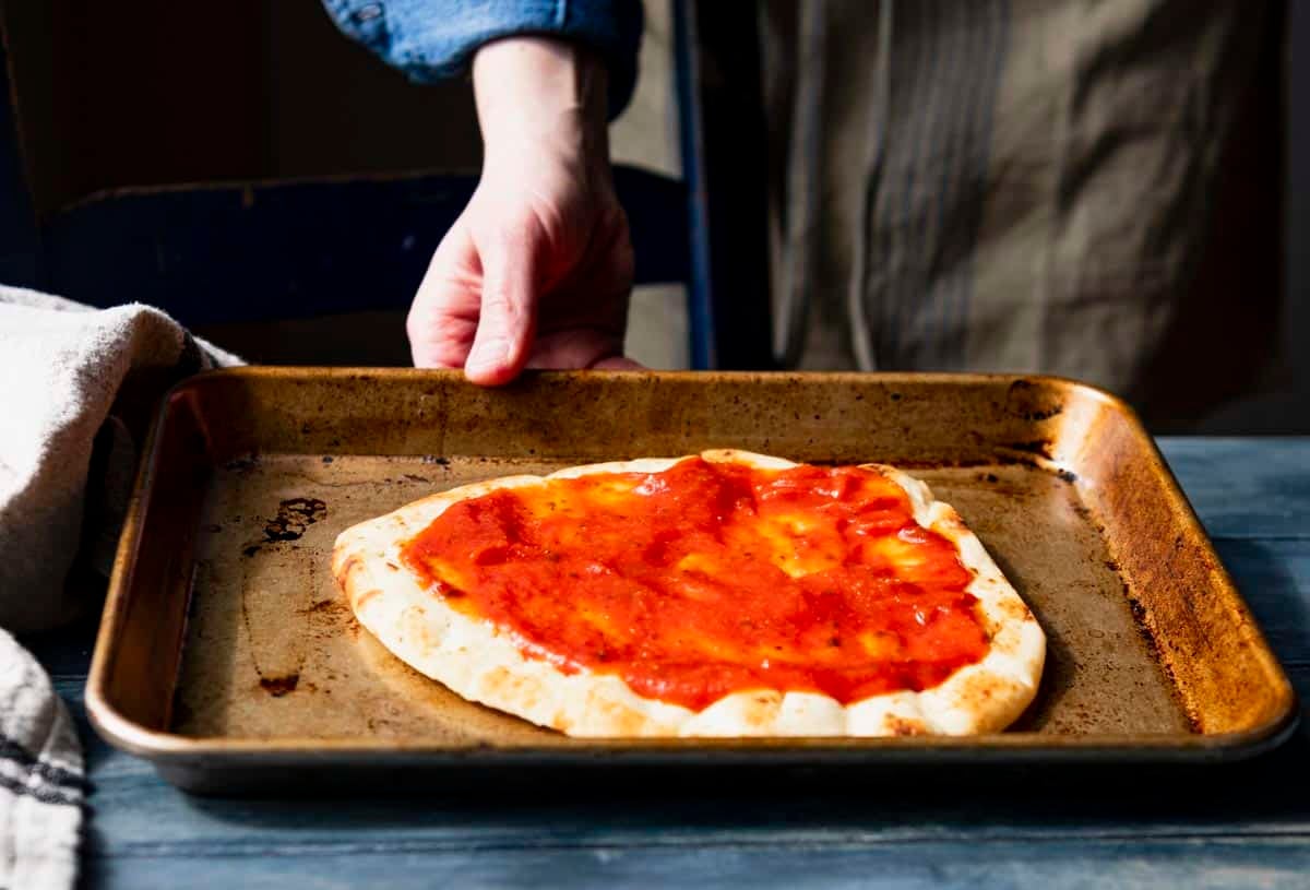 Spreading pizza sauce on a naan flatbread pizza.