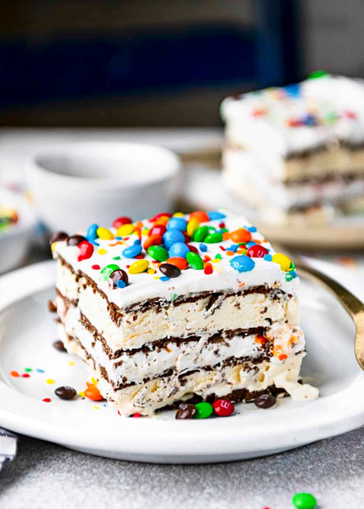 Side shot of ice cream sandwich cake on a white plate with mini M&Ms on top.