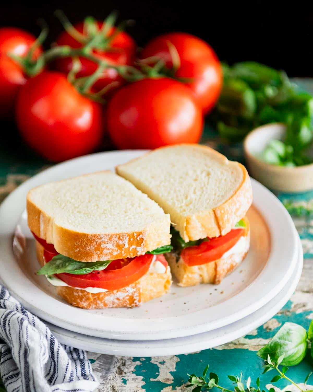 Side shot of a southern tomato sandwich on a white plate with fresh tomatoes and basil in the background.