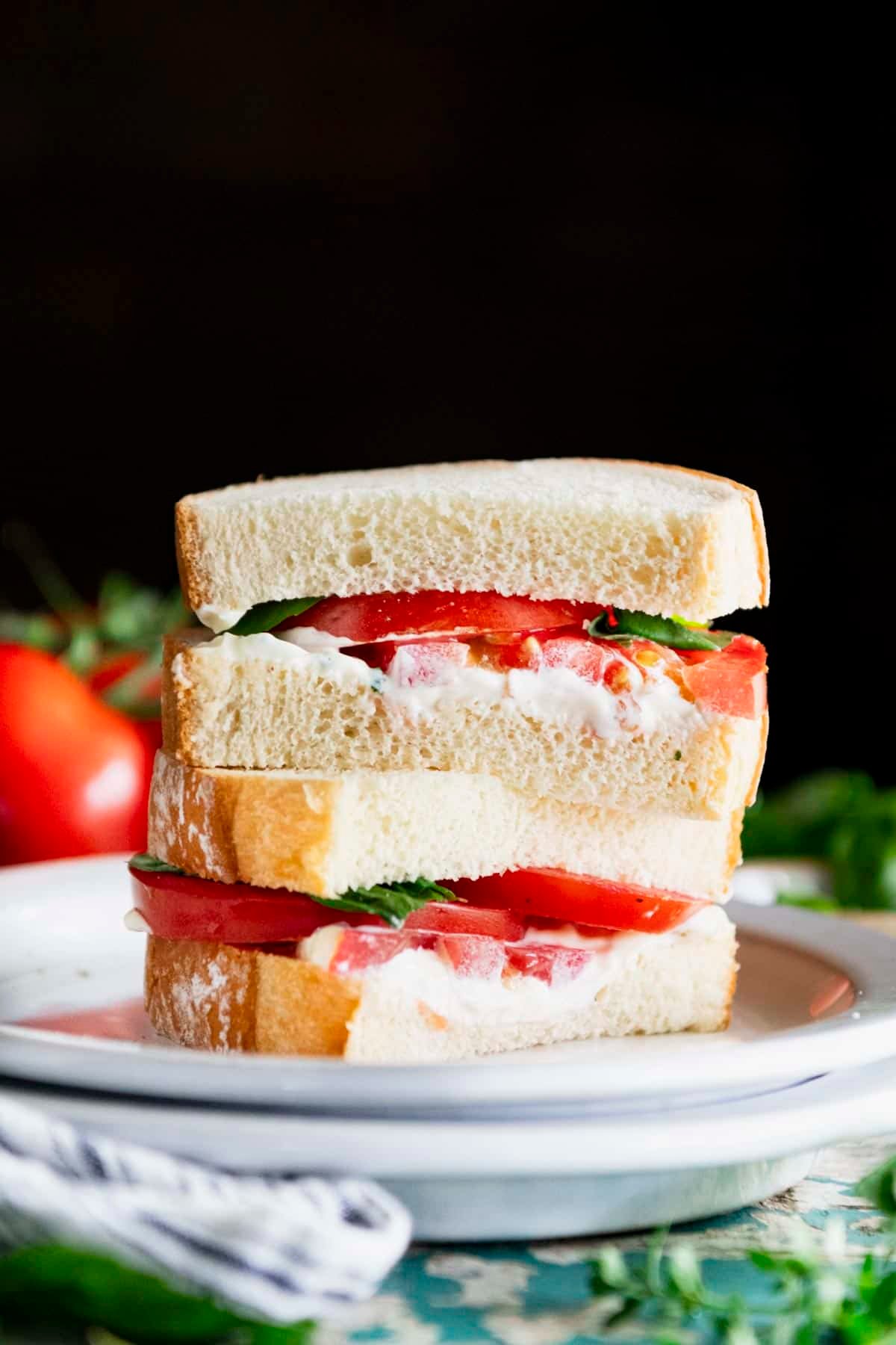 Side shot of a tomato sandwich stacked on a white plate.
