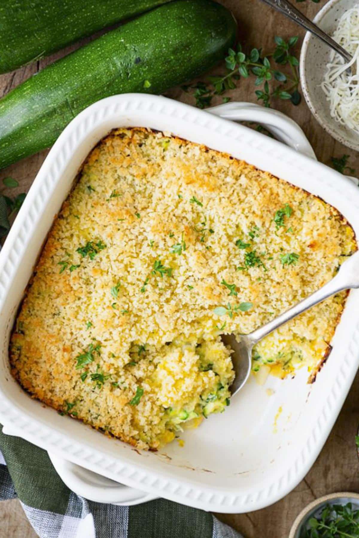Old fashioned zucchini casserole in a white dish on a wooden table.