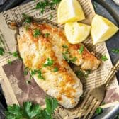 Square overhead shot of a garlic parmesan tilapia recipe on a plate with lemon wedges.