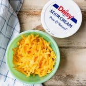Sour cream and a bowl of grated cheddar cheese.