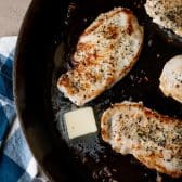 Basting chicken breast with melted butter in a cast iron skillet.